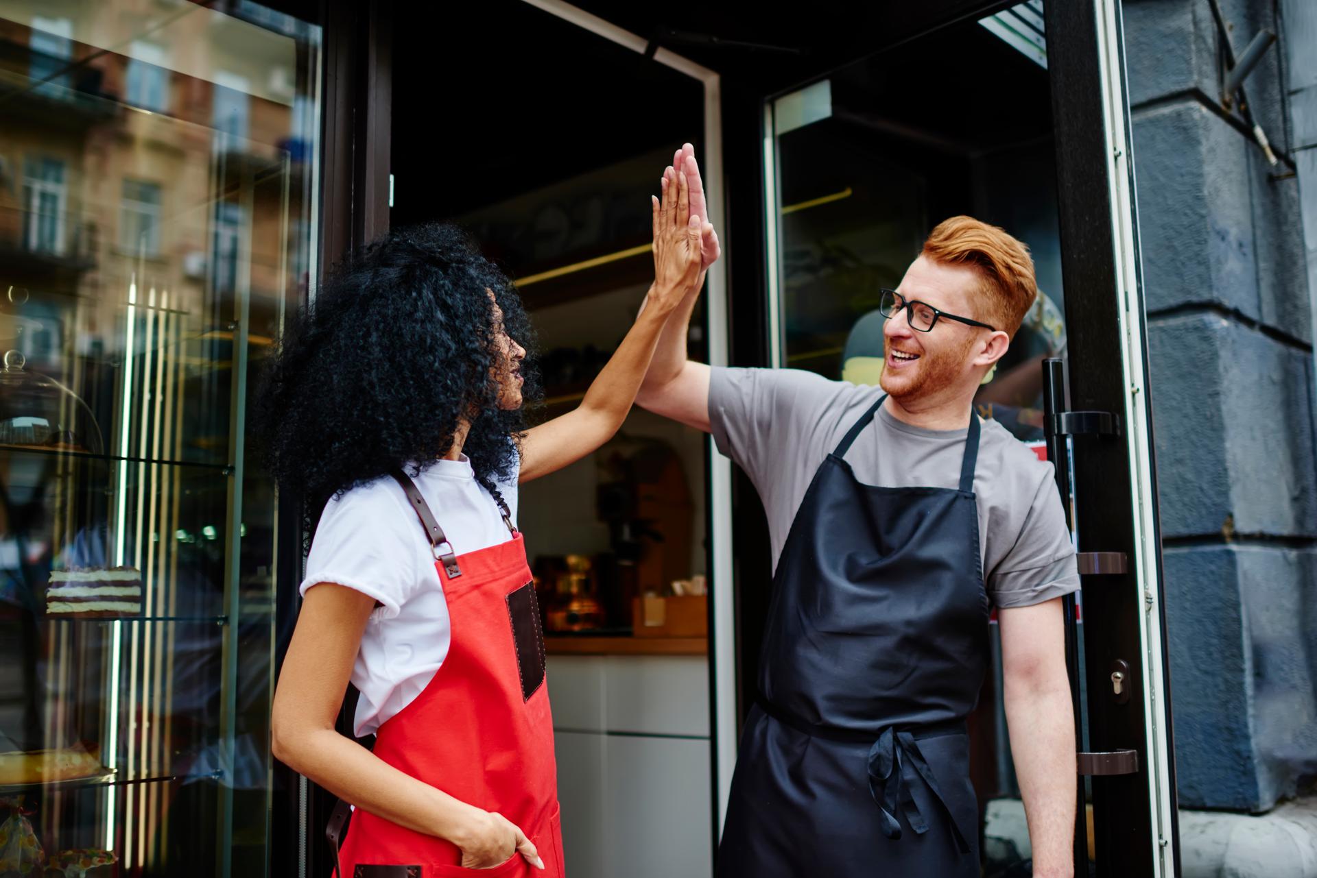 Satisfied multiethnic small business owners giving high five gesture at entry of cafe